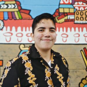 A person with short dark hear standing in front of a mural