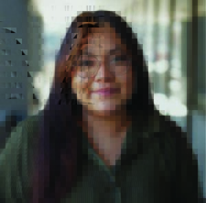 A woman wearing classes and a green button up top smiles.