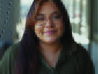 A woman wearing classes and a green button up top smiles.