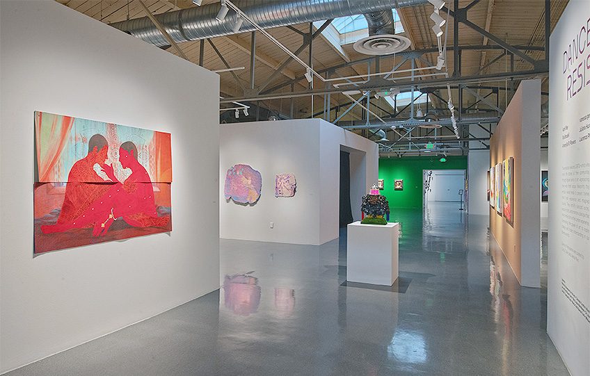 An art gallery with paintings and a central art piece on display, featuring exposed ceiling elements.
