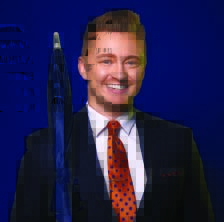 A man with short blonde hair and an orange tie holding a closed umbrella on his shoulder