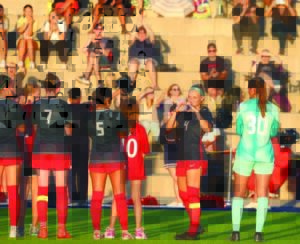Soccer players line up with the backs to us. One player turns and smiles at the camera.