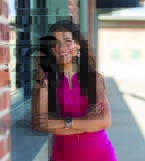 Woman in a pink dress leans against a brick wall.