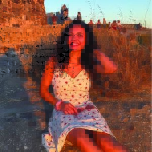 A woman with long dark hair and wearing a white dress sit in a sunset.