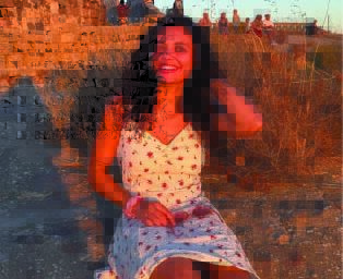 A woman with long dark hair and wearing a white dress sit in a sunset.