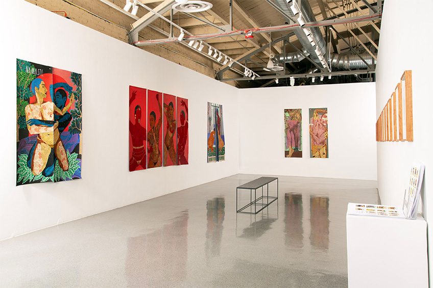 Art gallery room with colorful paintings on white walls and a black metal bench.
