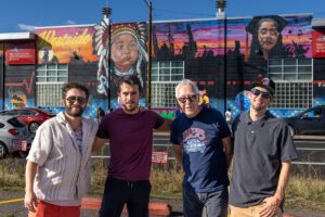 Four men pose in front of a mural