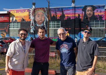 Four men pose in front of a mural
