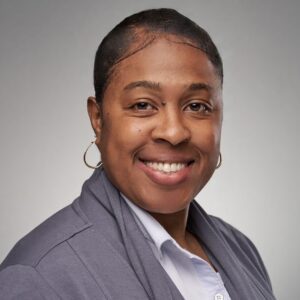 A woman with black hair wearing hoop earrings and a gray blazer