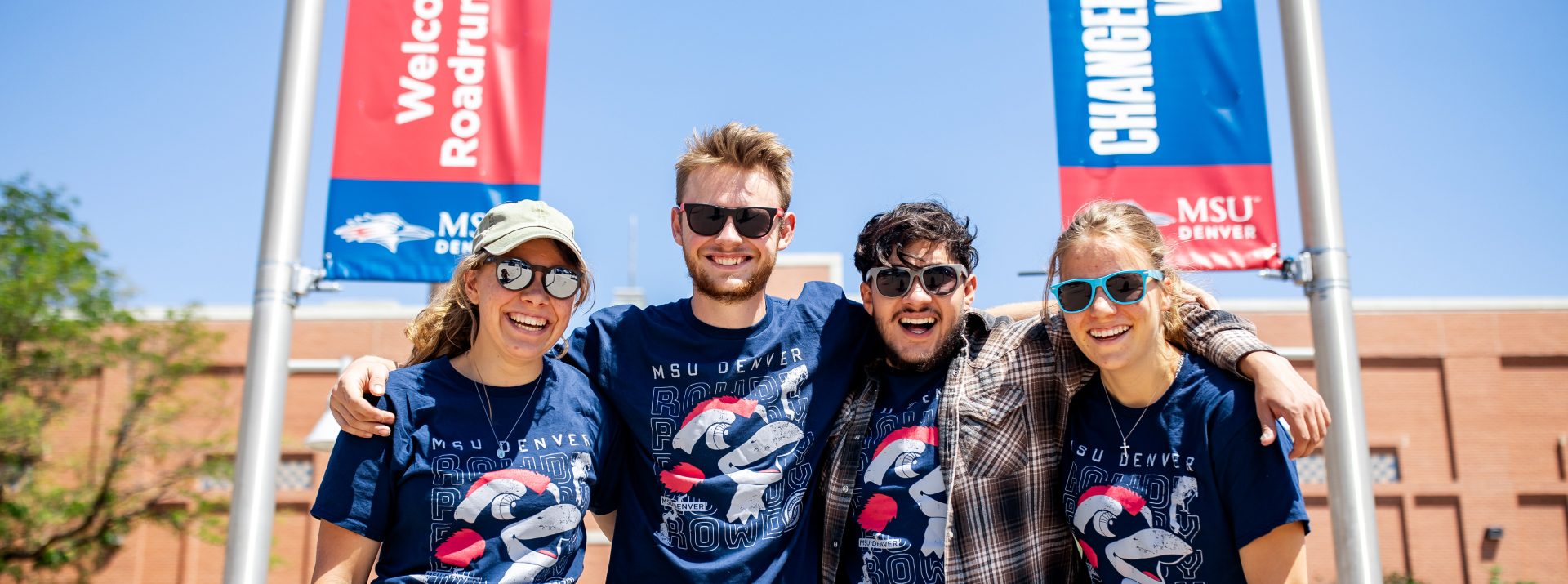 Four students in matching MSU Denver shirts standing together on the JSSB lawn during Welcome Week 2025