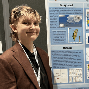 A person with blonde hair wearing a brown blazer stands in front of a presentation