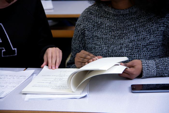 Two students flip through the pages of a workbook together