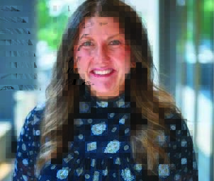 Woman with long brown hair and is wearing a light blue and dark blue spotted shirt.