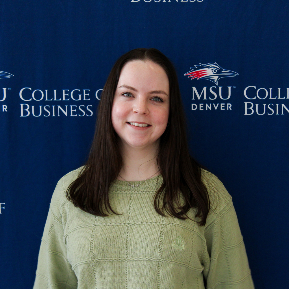 A student ambassador in a light green textured sweater smiling in front of an MSU Denver College of Business backdrop.