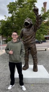 Photo of Caleb in front of the Rowdy statue