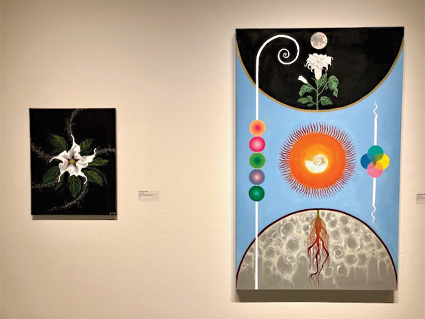 Two paintings in a gallery: one with a white flower, the other with abstract colorful elements including a sun-like shape and spheres.