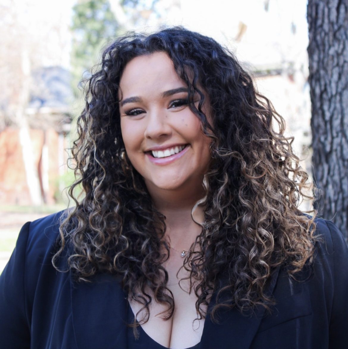 woman with curly hair smiling wearing black blazer