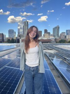 Joleen on a roof with solar panels in front of the denver city skyline