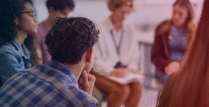 a group of young adults gather in a circle, talking, while a therapist takes notes with a blue and red gradient overlay over the image