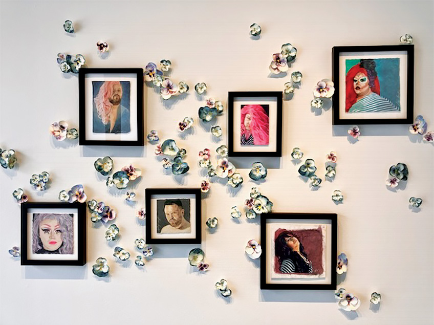 A wall with seven framed portraits surrounded by ceramic flowers.