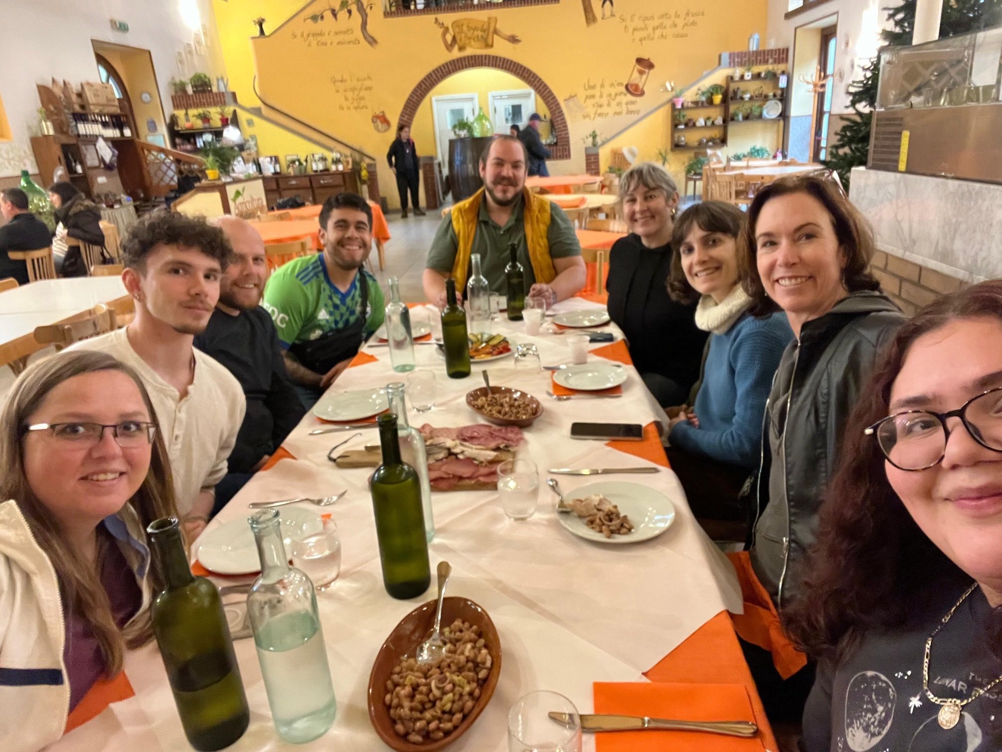 A group of nine friends smiling around a long restaurant table filled with platters of food in Rome.