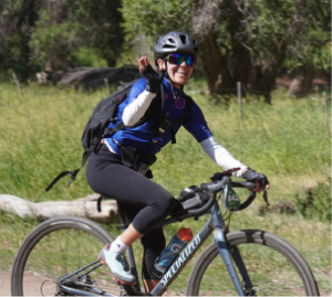 A woman waves at the camera while on her bicycle