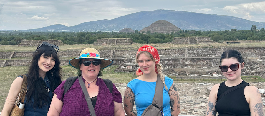 Four people pose for a picture in front of ancient ruins in Mexico.