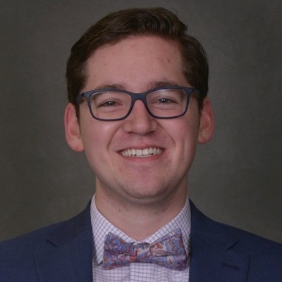 Man wearing classes and in white shirt, paisley bow tie, and dark blue jacket