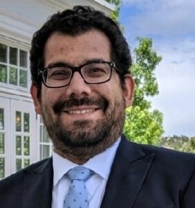 Man wearing glasses in white shirt, blue tie, and black jacket