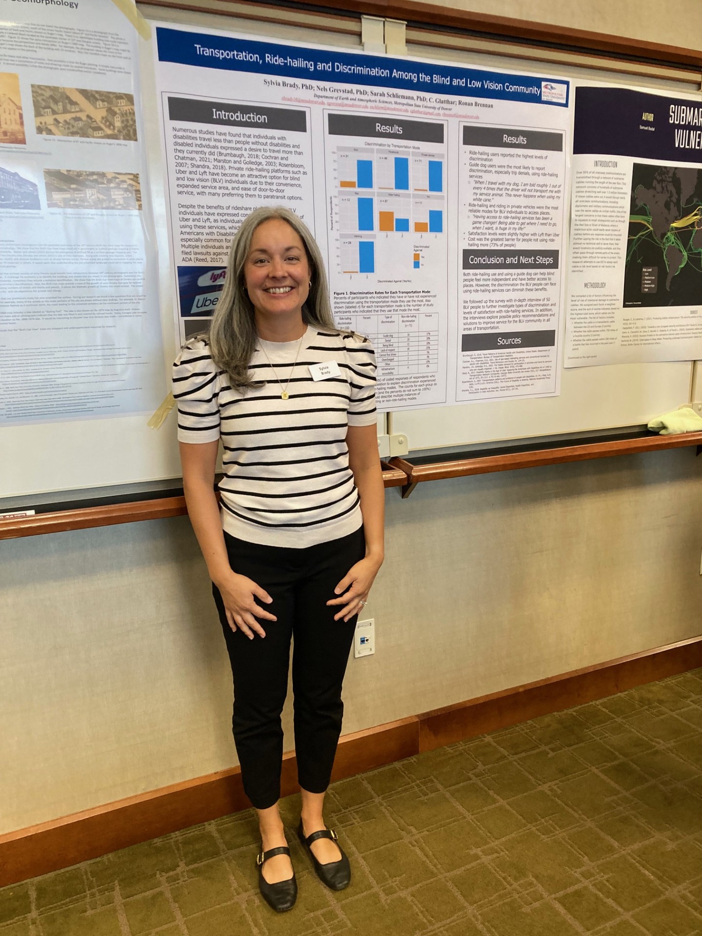 A woman with gray hair and a striped shirt standing in front of a research-focused poster.