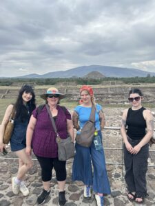 Four people posing with archaeological ruins in the distance.