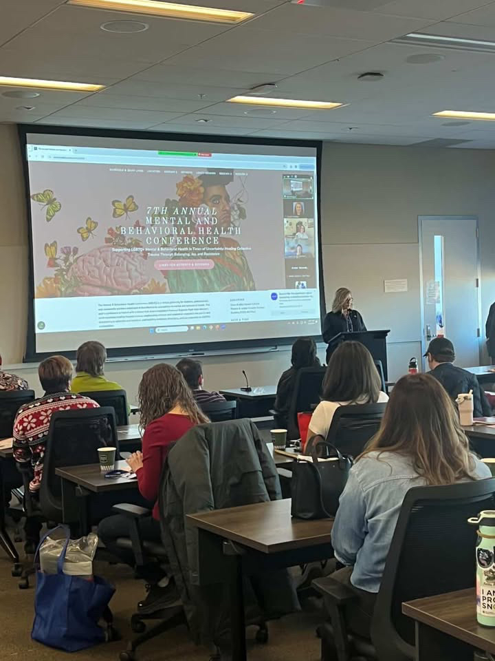 Classroom scene with several individuals sitting and engaging with a projector screen at the front.