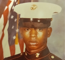 Man with a white military hat in front of an American flag