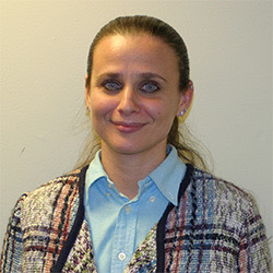 Woman with a blonde pony tail dressed in a blue collared shirt and plaid jacket