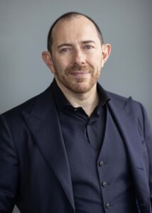 Man in black shirt, vest, and jacket