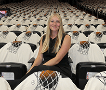 A woman with long blonde hair sits in the stands of a basketball arena