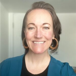 Woman in black shirt, blue blazer and gold hoop earrings