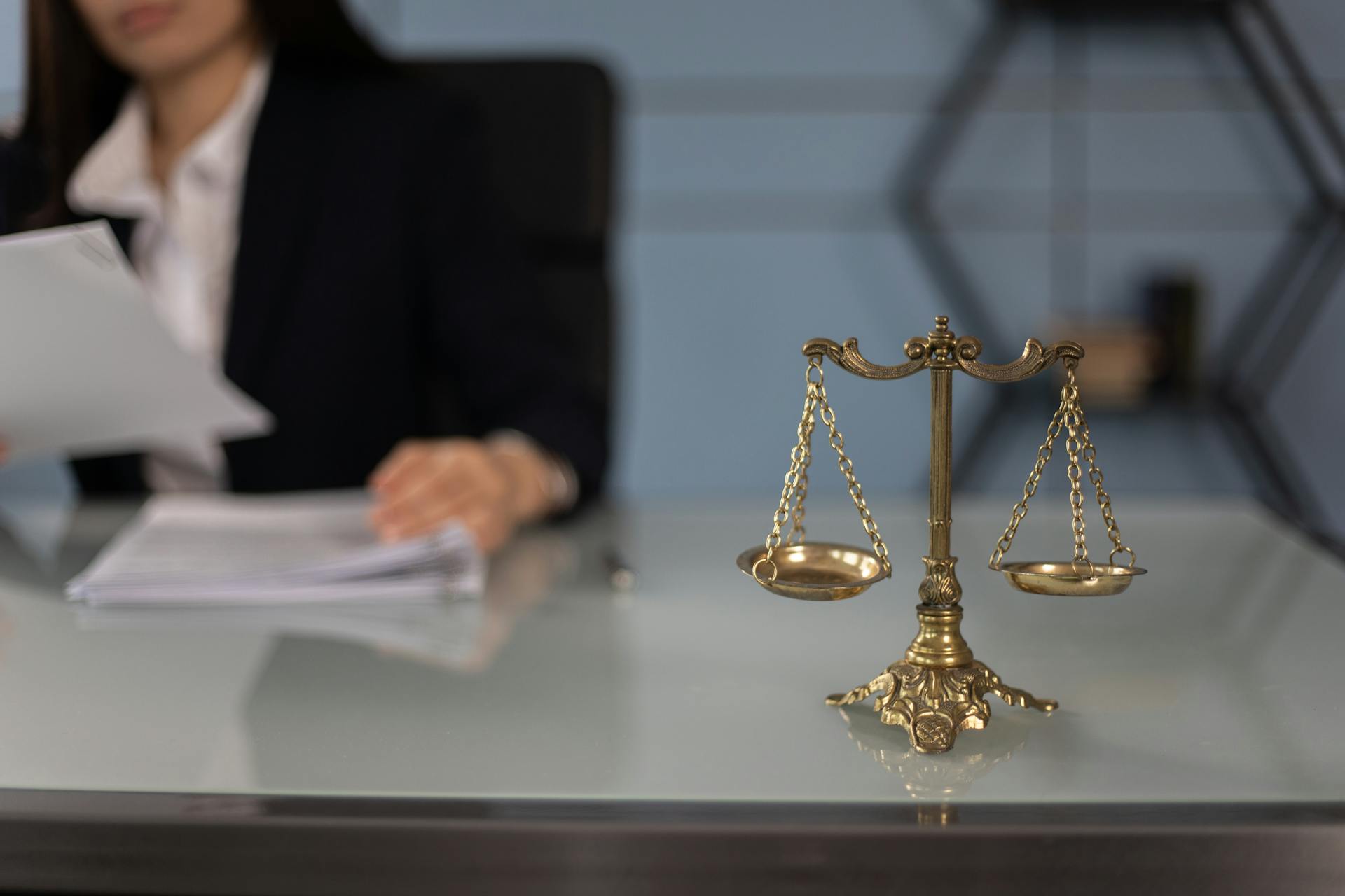 A golden scale typically associated with law (Scales of Justice) sits on a desk with a lawyer reviewing a document.