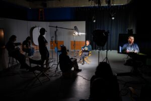A video recording studio with crew and a woman being interviewed.