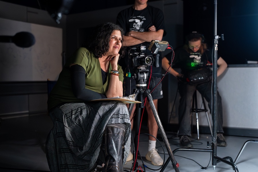 A woman sitting in a director's chair with two crew members in the background.