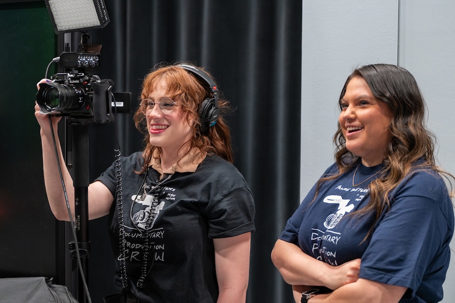 Two women, one holding a camera and wearing headphones.