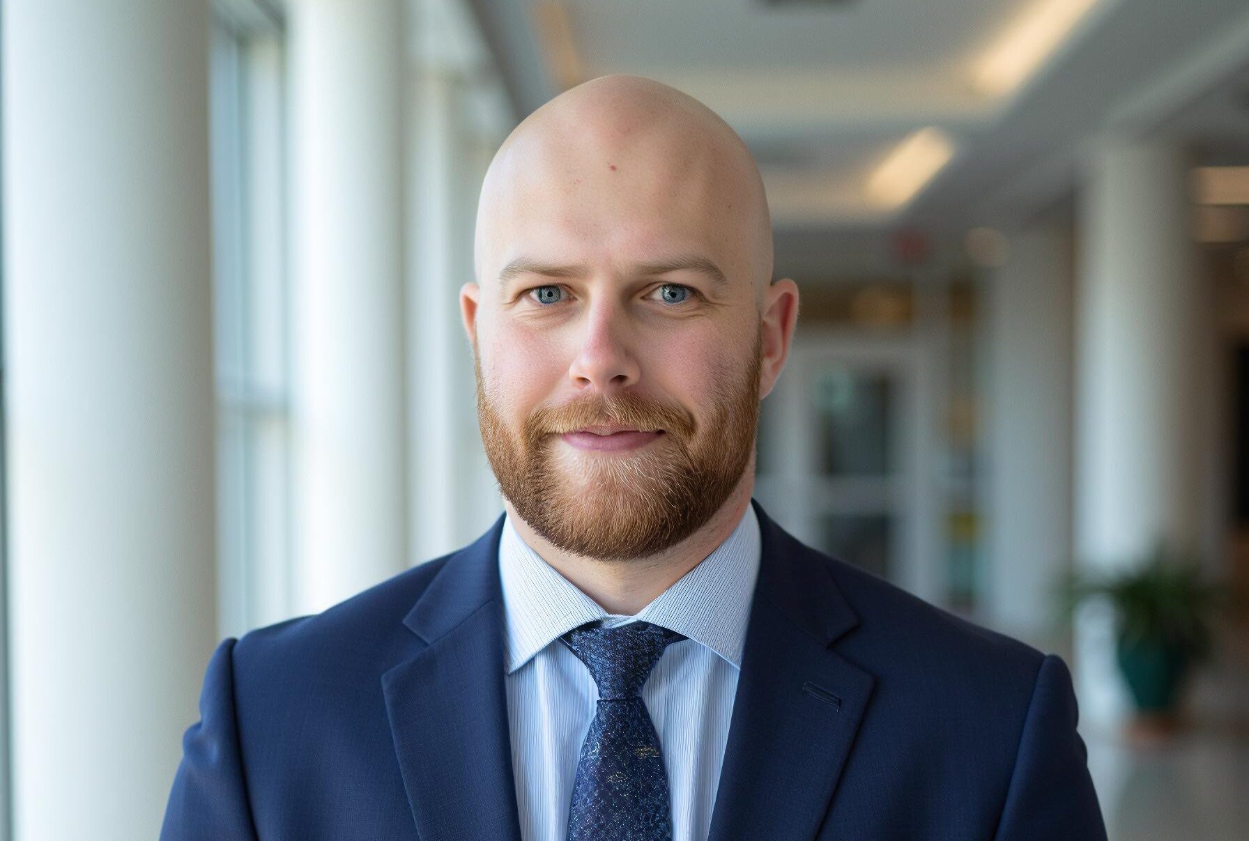 Man in a blue suit and tie poses for a photo with a blurred depth of field background