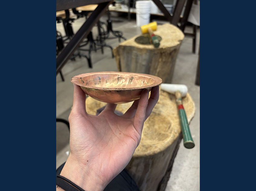 Lizeth is holding a brass metal that is sunk in to create a bowl shape.