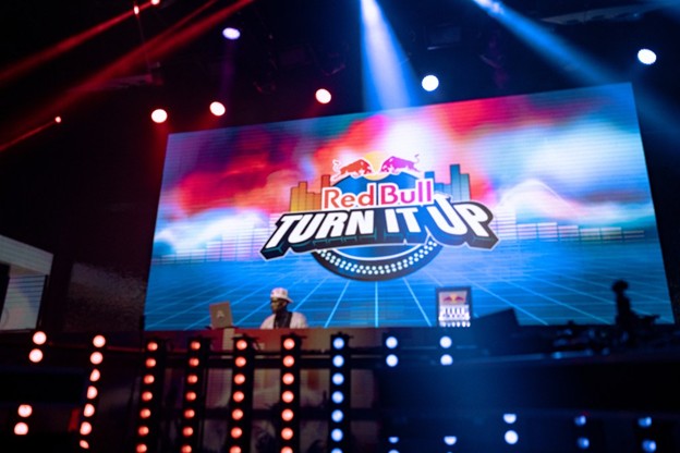 DJ in concert sitting in front of a screen with the Red Bull: Turn It Up logo