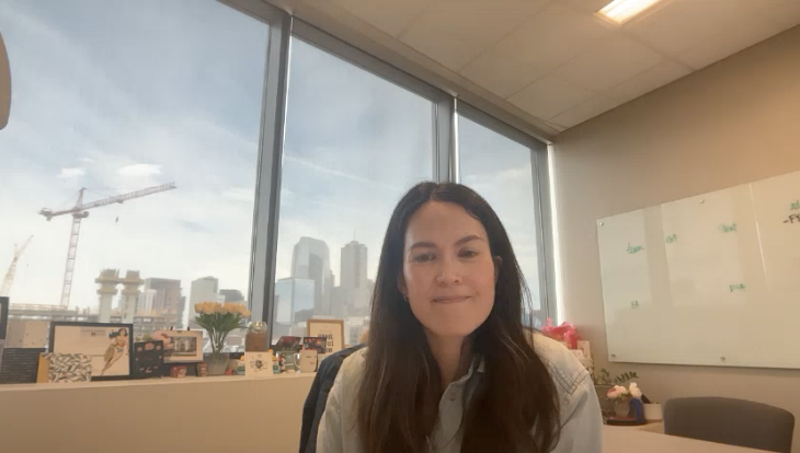 Kaycee Gerhart sitting in her office with the Denver skyline behind