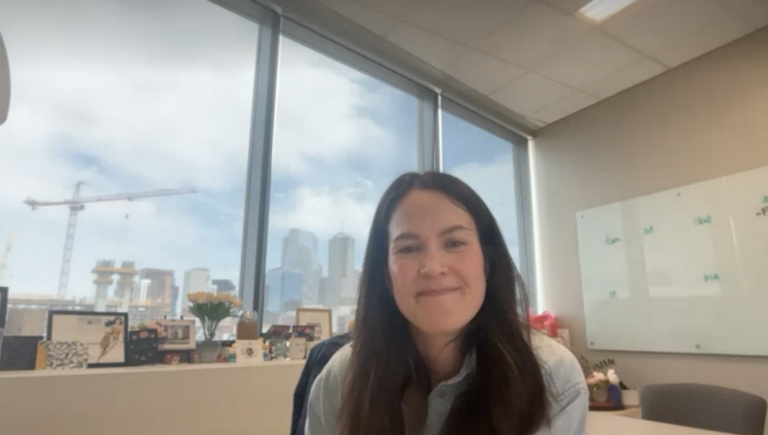 Kaycee Gerhart sitting in her office with the Denver skyline behind