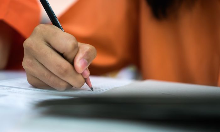 Close up image of a person's hand holding a pencil and filling in bubbles on an exam