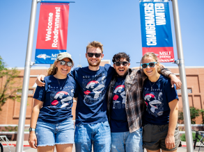 Four students standing on the Jordan Student Success Building lawn in the summer