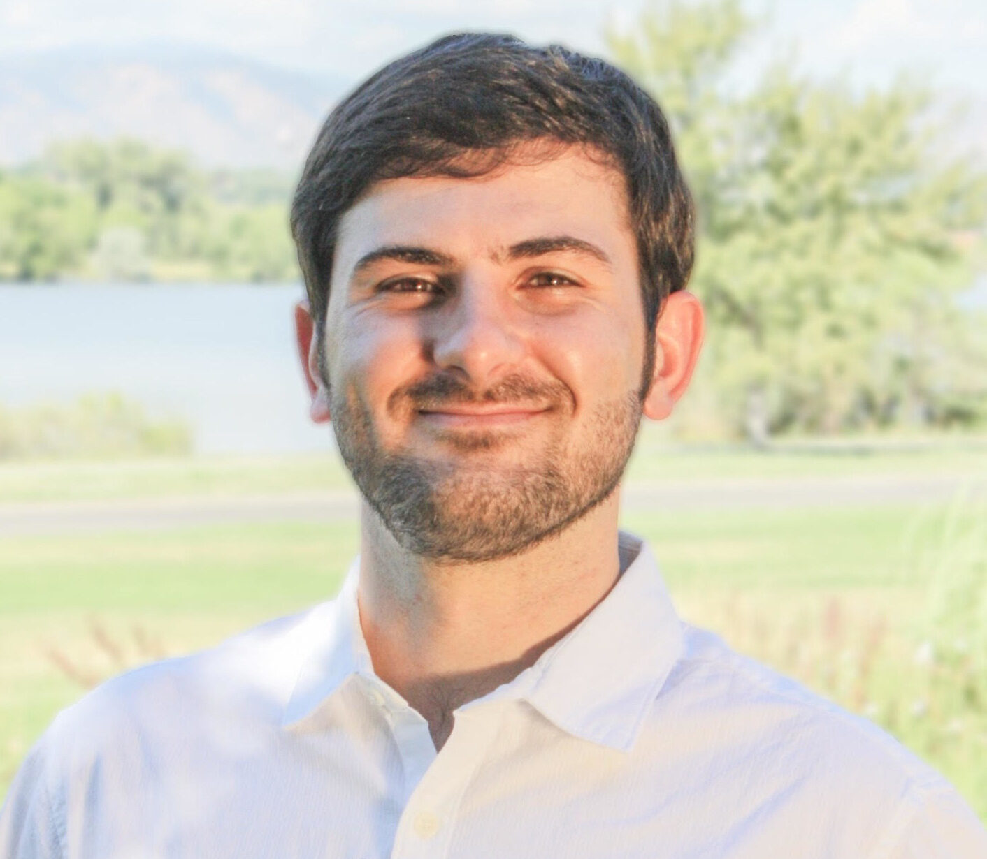Bright contrast photo of a male student wearing a white collared shirt in front of an outdoor scenery.