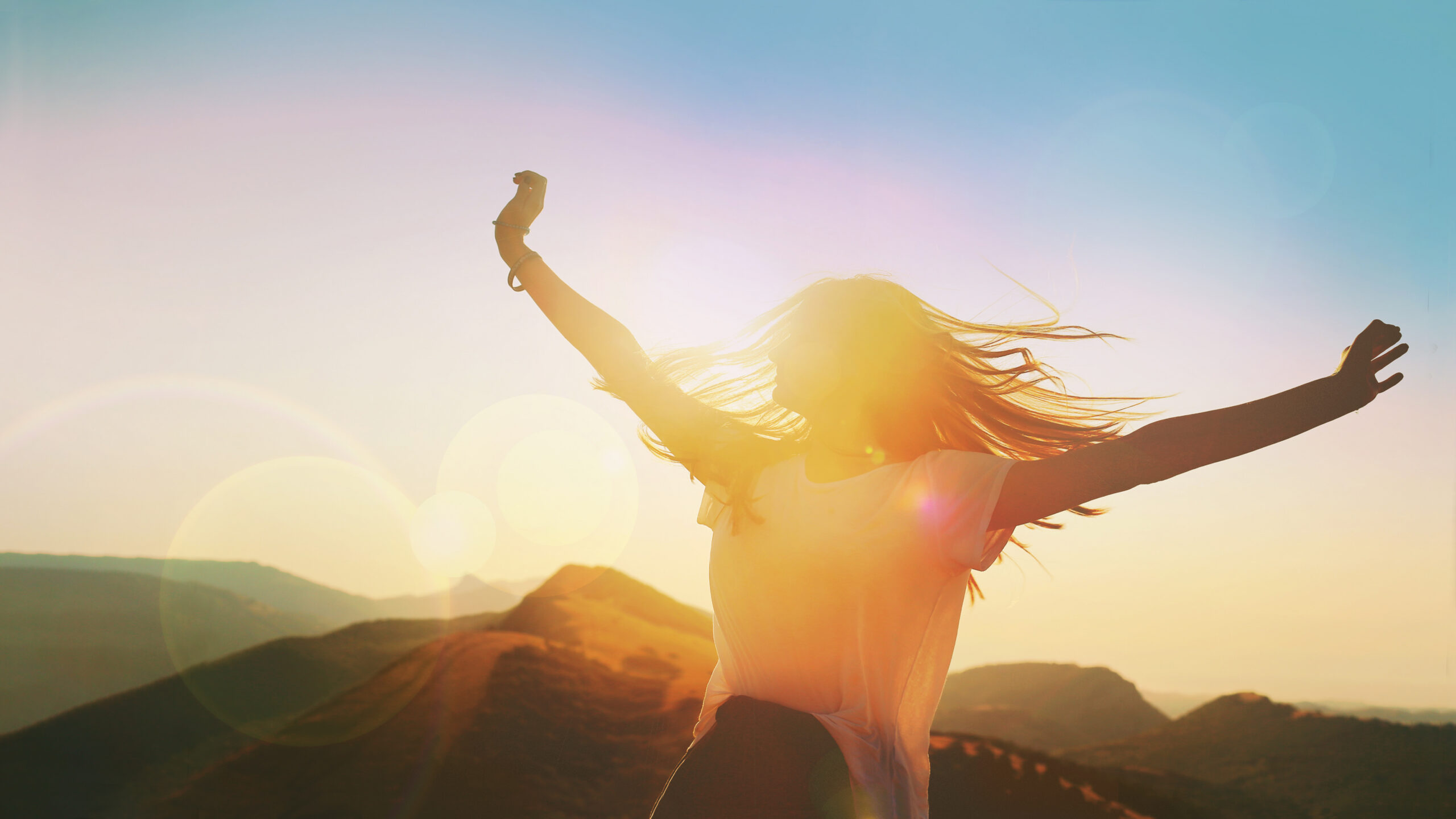 A happy woman who is standing on top of a mountain with her hands in the air.